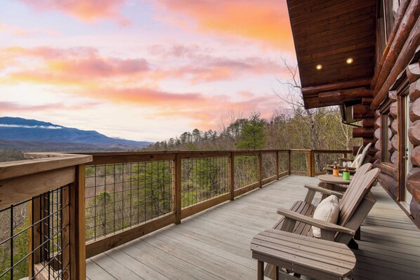 A wooden deck with a railing, outdoor seating, and a view of mountains and trees. - Sleeps 21 Luxury Cabin w/ Panoramic View, Hot Tub, Game Room Pinnacle Chalet (Gatlinburg)