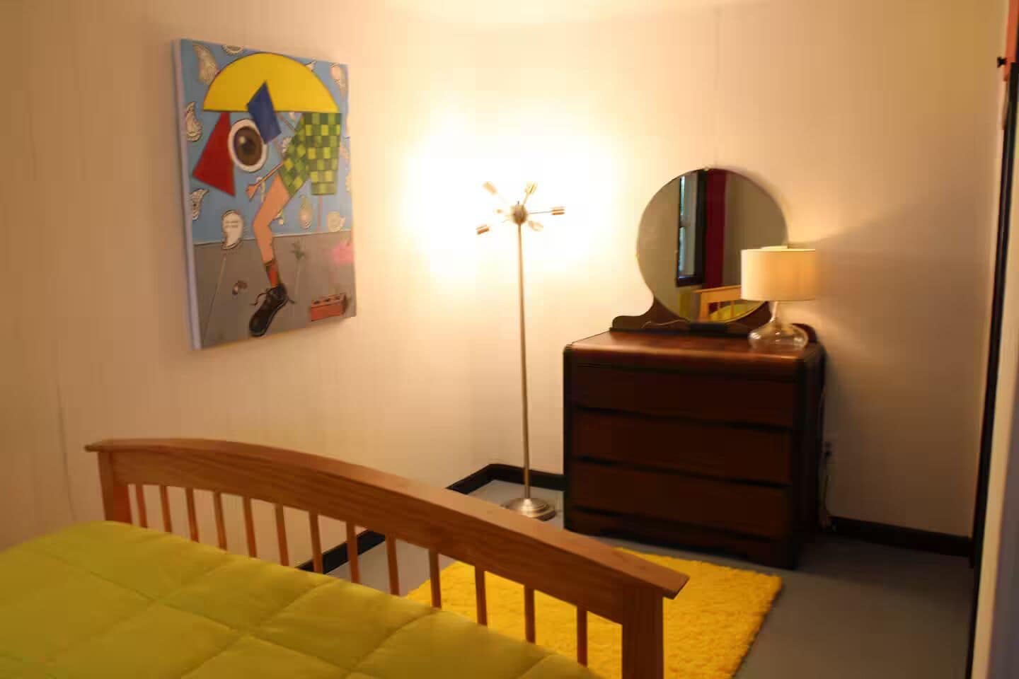 A bedroom with a bed, a dresser, a lamp, and a wall-mounted painting.
