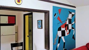 Une pièce avec un mur blanc, un tableau abstrait bleu, une chaise rouge et une porte jaune.