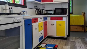 Une cuisine de taille réduite avec des meubles blancs, un four à micro-ondes, une cuisinière et un tapis aux couleurs vives.