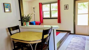Un coin repas avec une table ronde et des chaises, une fenêtre avec des rideaux rouges et une plante en pot.