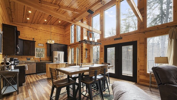 A log cabin interior with a dining area, kitchen, and seating space.