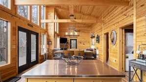 A wooden cabin interior with a kitchen area featuring a stainless steel island, wooden cabinets, and a dining table with chairs.