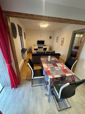 A dining area with a table set for four, a sofa, a TV, and a clock on the wall.