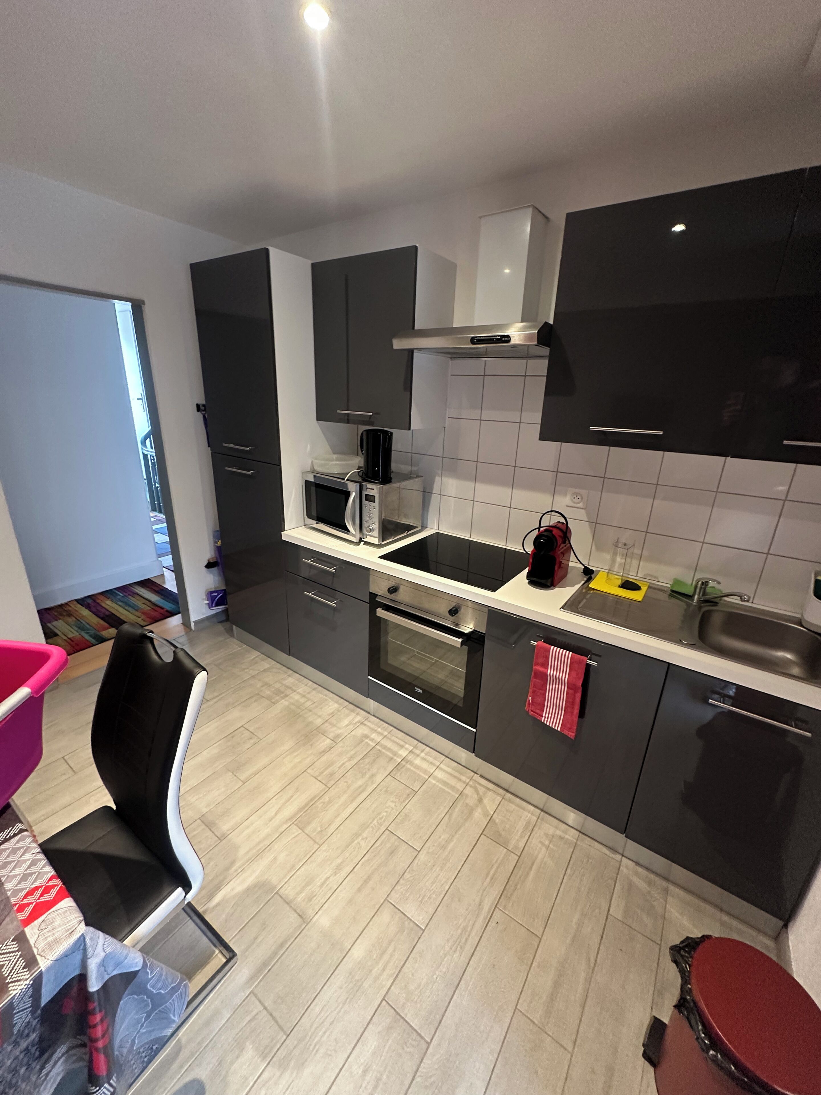 Una cucina moderna dotata di forno a microonde, forno e lavello. Si nota una sedia e un tavolo con una tovaglia decorata.
