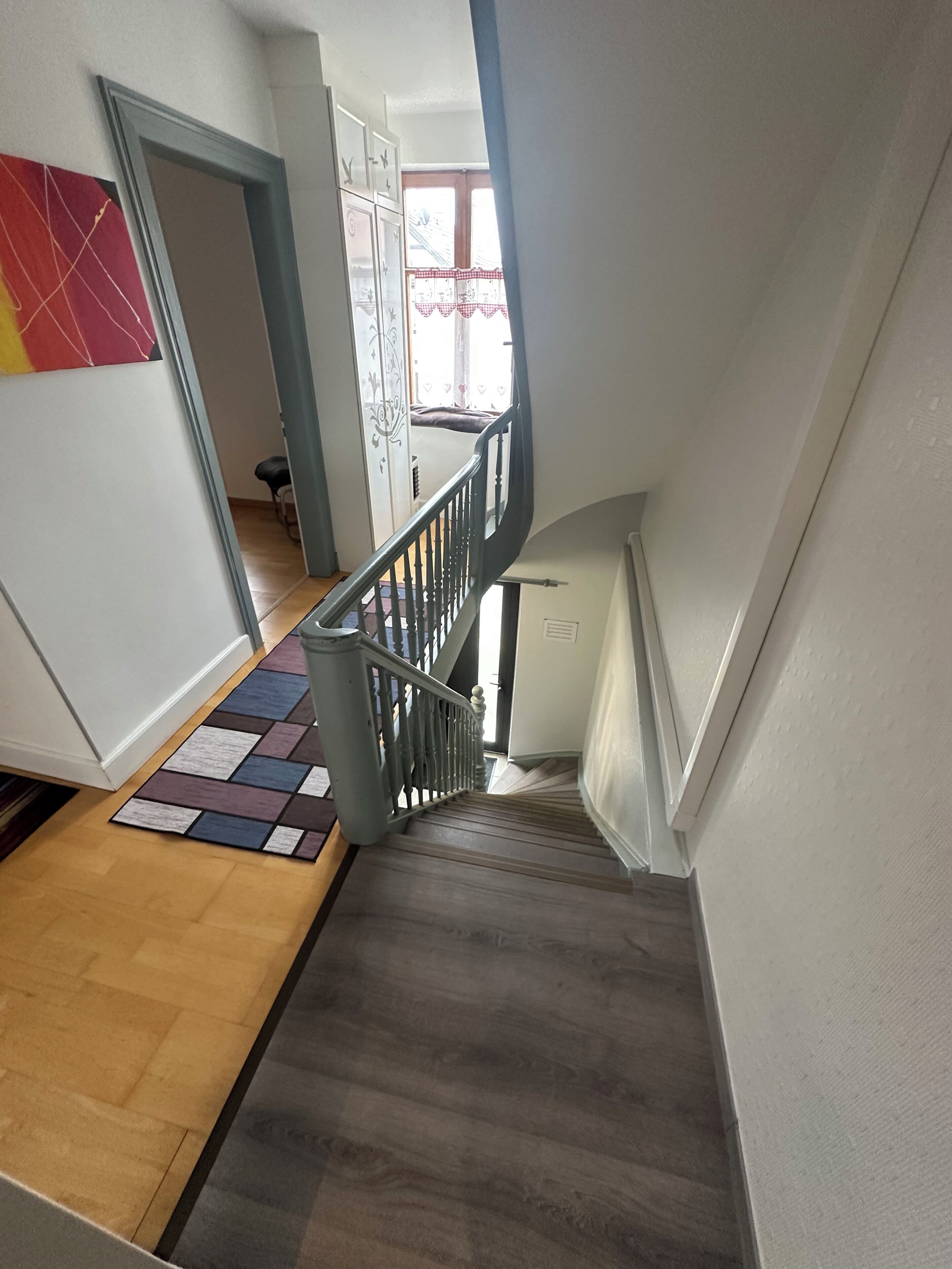 Un escalier avec des marches recouvertes de bois, une rampe en métal et un tapis à motifs au bas de l’escalier.