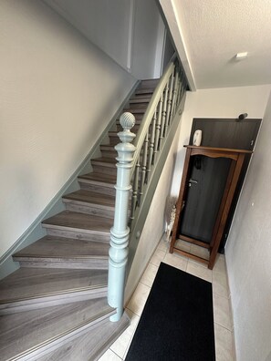 A staircase with wooden steps and a white balustrade, leading to a dark wooden door with a small shelf above it.