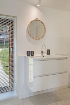 A modern bathroom with a white vanity, a round mirror, and a faucet.