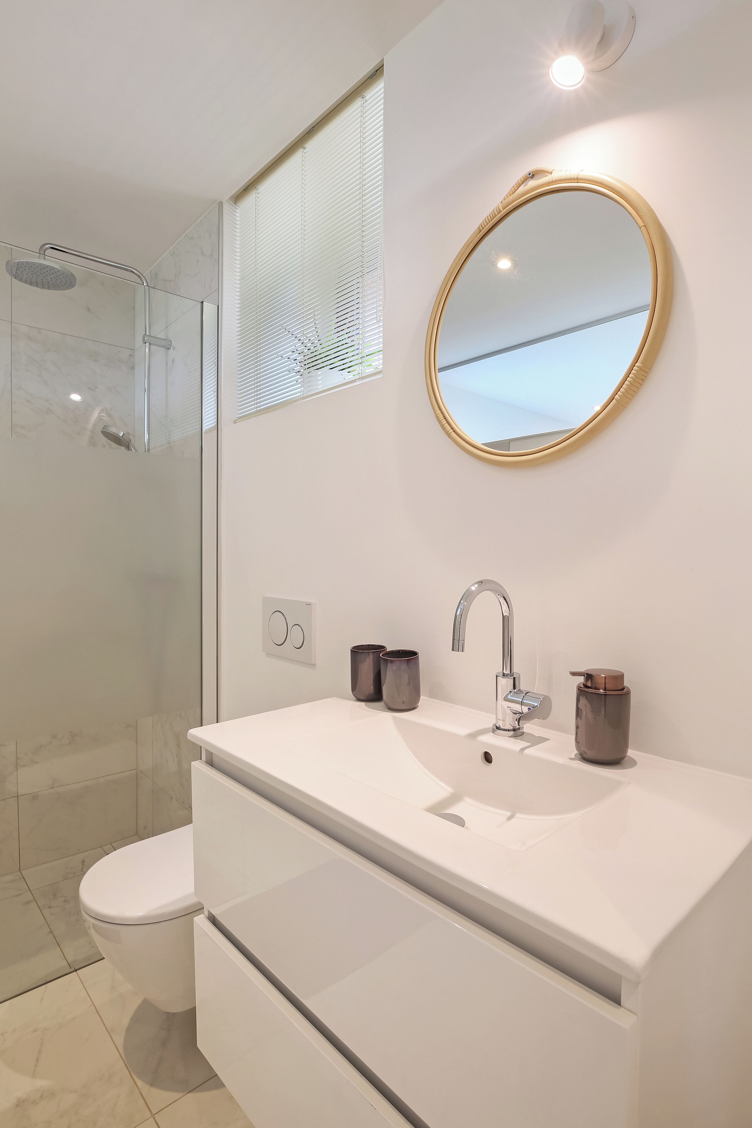 Un baño moderno con cabina de ducha de vidrio, un lavabo blanco y un espejo con marco dorado, además de un inodoro.