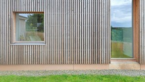 A modern building with vertical wooden siding, a small window, and a glass door. - Le pré de Régine et Joseph (Malmedy)