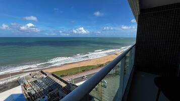 Vista de uma varanda para uma praia com ondas, um estacionamento e painéis solares.