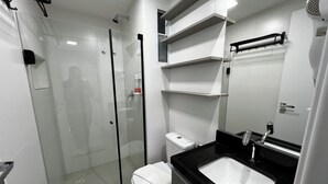Ein modernes Badezimmer mit einer Duschkabine, einer weißen Toilette und einem schwarzen Waschbecken mit Spiegel darüber.