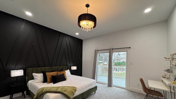 A modern bedroom with a large bed, a desk, and a balcony.