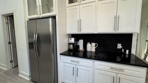 A modern kitchen with white cabinets, a stainless steel refrigerator, and a black countertop.