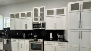 A modern kitchen with white cabinetry, a stainless steel oven, a microwave, and a black countertop.