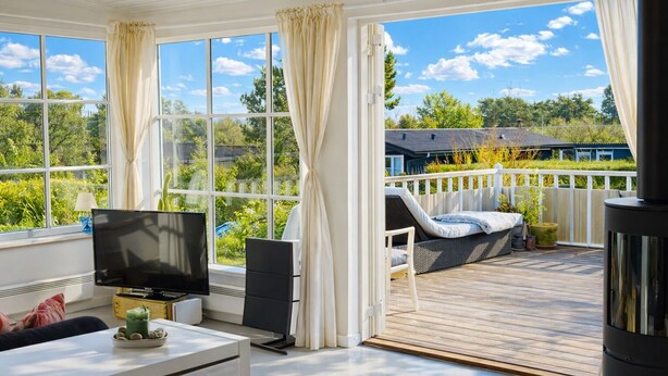 Una habitación iluminada por el sol con televisor, sofá y terraza con mobiliario exterior.