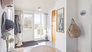 Una habitación luminosa y bien iluminada con un gran ventanal corredera que da a un espacio exterior. Hay dos espejos en la pared, un bolso colgado y un jarrón con flores.