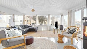 Una sala moderna con un sofá seccional, una chimenea y grandes ventanales con vistas al exterior.