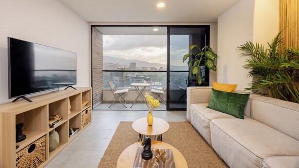 Ein modernes Wohnzimmer mit Flachbildfernseher, einer Couch, einem Couchtisch und einem Balkon mit Blick auf die Stadt.