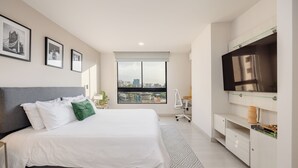 Ein modernes Hotelzimmer mit einem großen Bett, Blick auf die Stadt, einem Flachbildfernseher und einem Schreibtisch mit Stuhl.