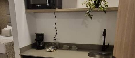 Una kitchenette compacta con microondas, cafetera y un lavamanos pequeño.