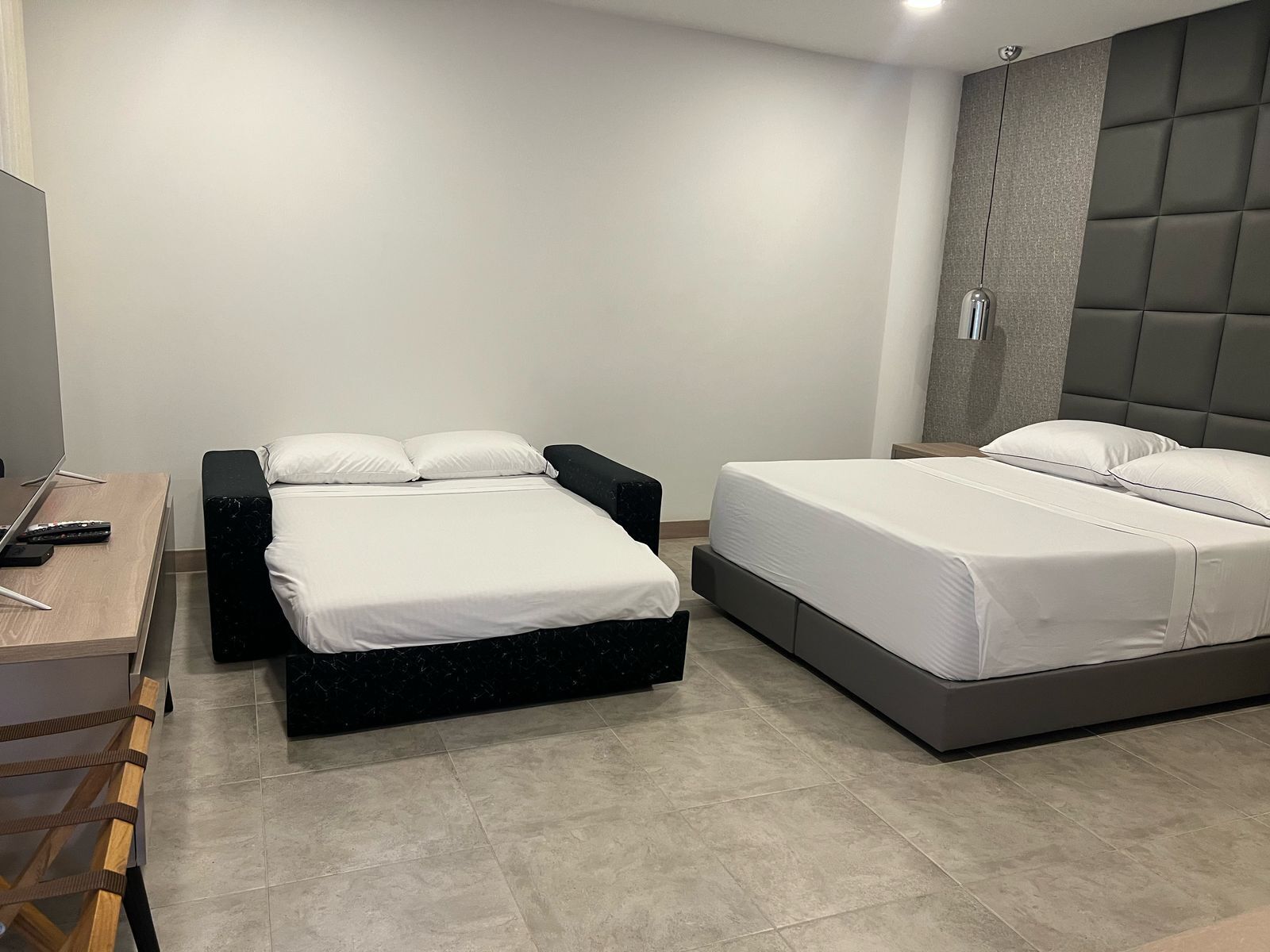 A modern hotel room with a bed, bedside table, and a desk with a chair.