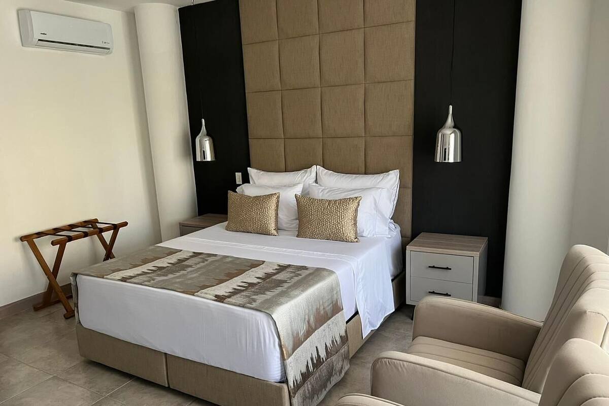 A bedroom with a bed, bedside tables, a chair, and an air conditioning unit.