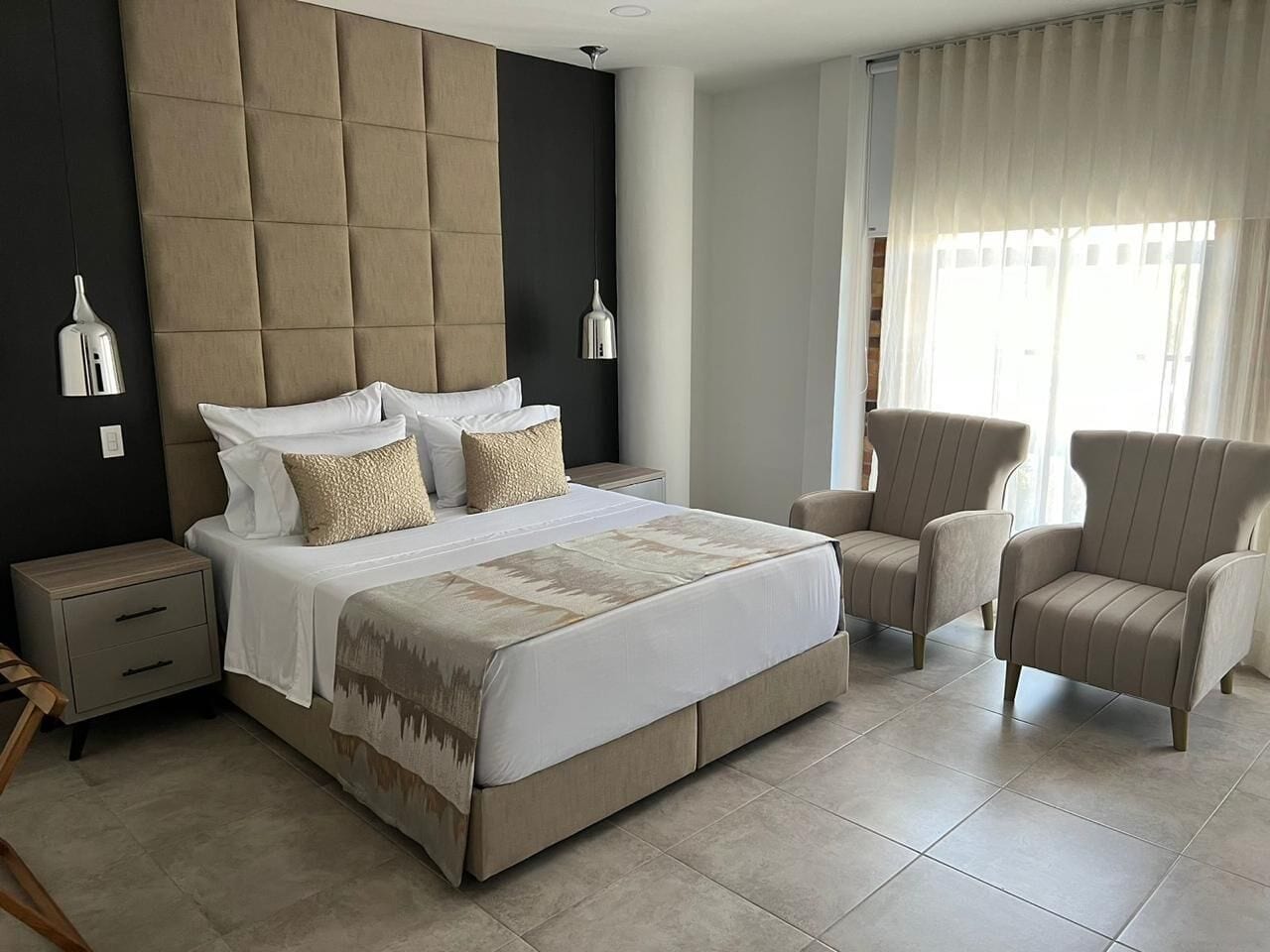 Une chambre à coucher avec un grand lit, deux tables de chevet, une chaise et une fenêtre avec des rideaux.