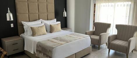 Un dormitorio con una cama grande, dos mesitas de noche, una silla y una ventana con cortinas.