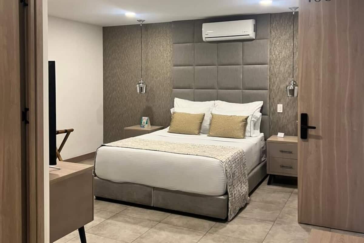 A modern bedroom with a large bed, bedside tables, an air conditioning unit, and a door with the number 406.
