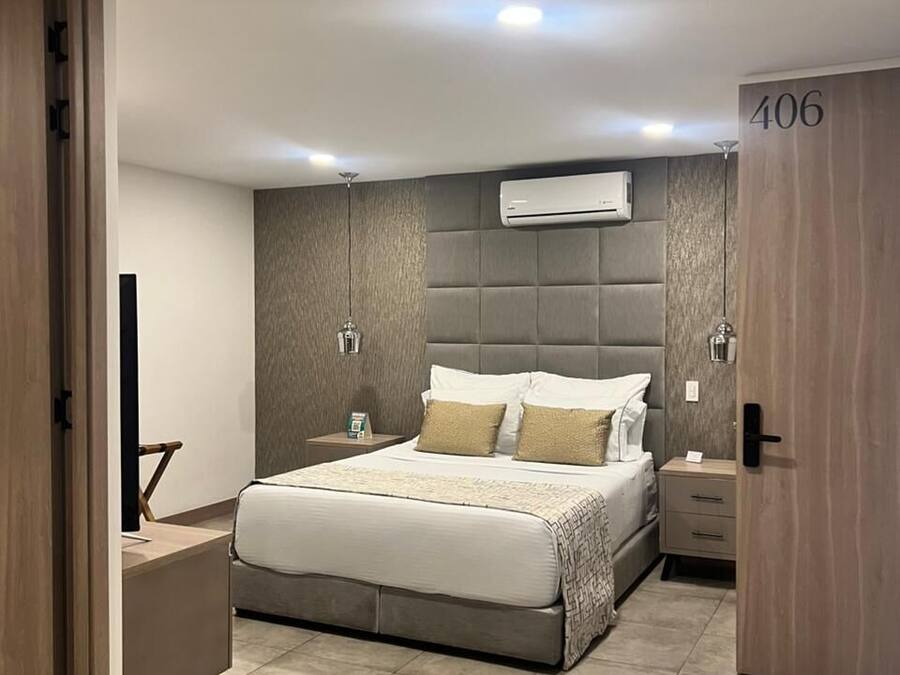 Quarto moderno com uma cama grande, mesas de cabeceira, ar condicionado e uma porta com o número 406.