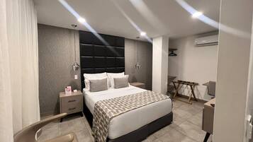 Un dormitorio moderno con una cama, mesitas de noche, una silla, un escritorio y un equipo de aire acondicionado.
