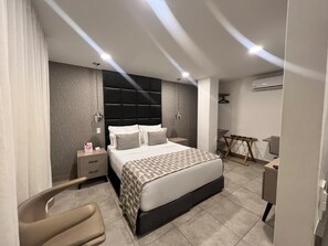 A modern bedroom with a bed, bedside tables, a chair, a desk, and an air conditioning unit. - HOTEL 45 PARK (Sabaneta)