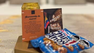 Una tarjeta de bienvenida, un folleto del hotel y una bolsita de snacks sobre una mesa.