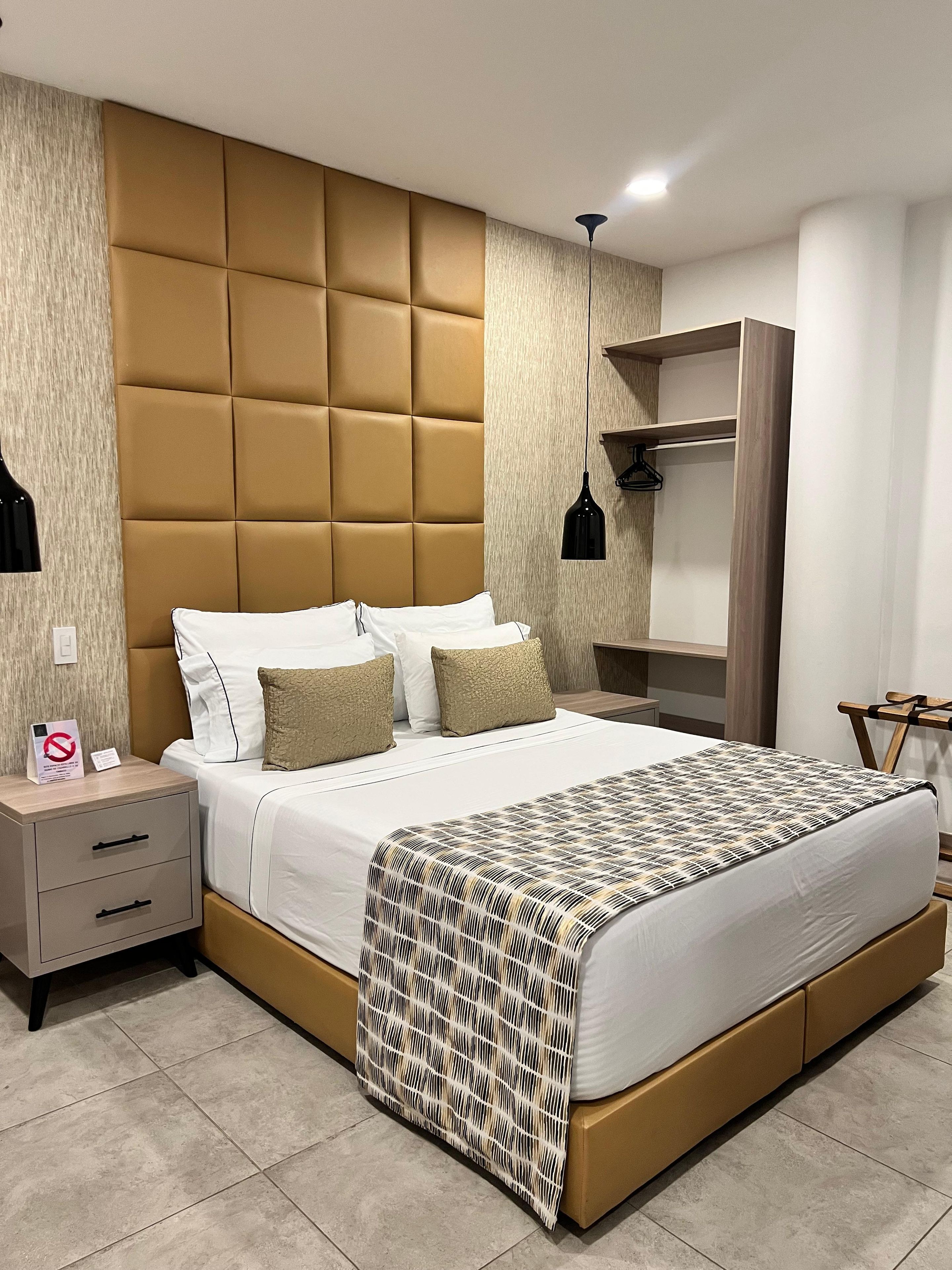 Una habitación de hotel moderna con una cama grande, una mesita de noche, un armario y una lámpara colgante.