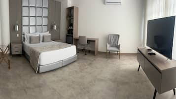 A modern hotel room with a bed, desk, chair, TV, and air conditioning unit.