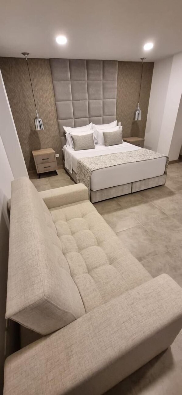 A modern bedroom with a large bed, a nightstand, a bench, and a ceiling light.