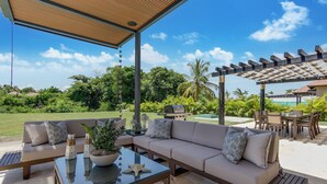 An outdoor patio with a sofa, a glass table, and a pergola. - Stylish Newly Built Villa in Cap Cana  (Punta Cana)