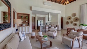 A spacious living area with a high ceiling, wooden beams, a sofa set, a coffee table, and a kitchen in the background. - Stylish Newly Built Villa in Cap Cana  (Punta Cana)