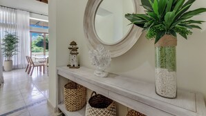 A hallway with a white console table, a round mirror, a potted plant, and wicker baskets. - Stylish Newly Built Villa in Cap Cana  (Punta Cana)