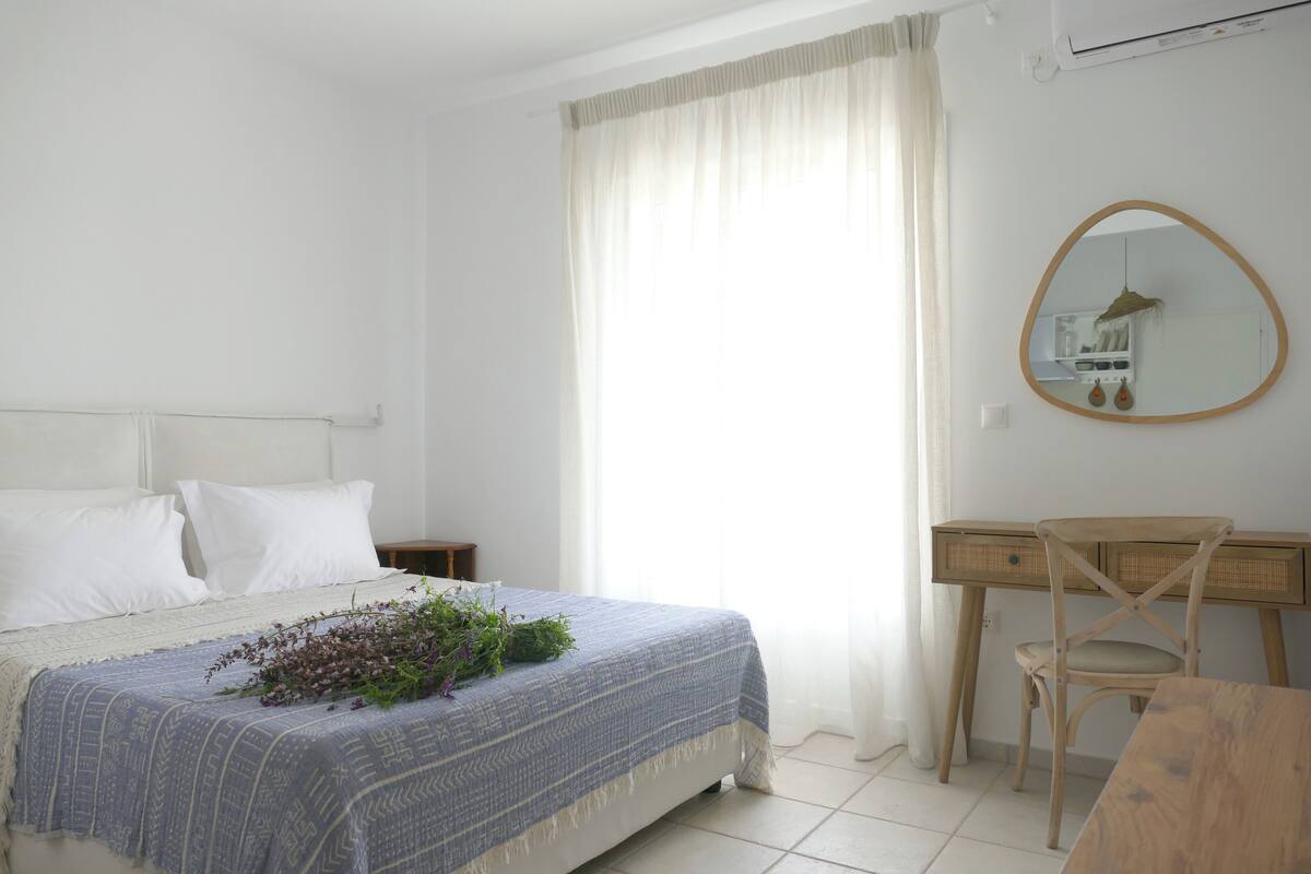A bedroom with a bed, a desk, a chair, and a mirror.