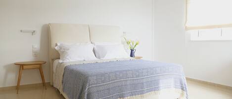 Un dormitorio con cama, mesita de noche y un jarrón con flores.