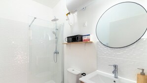 Un baño moderno con cabina de ducha de vidrio, inodoro, lavabo con espejo y estante con artículos de aseo.
