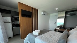 Ein modernes Hotelzimmer mit Bett, Schreibtisch, Flachbildfernseher, Küchenzeile und Meerblick.