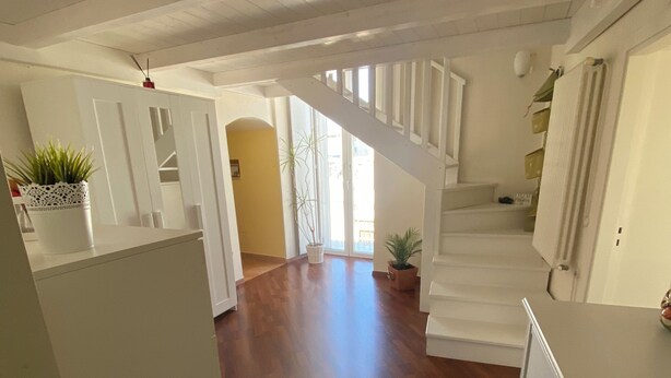 A spacious interior with a wooden floor, white walls, and a staircase leading to an upper level.