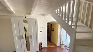 A spacious room with wooden flooring, a white staircase, and a door leading to another area.