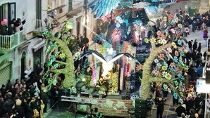 A street parade with a large, colorful float featuring a tree and skeleton figures.