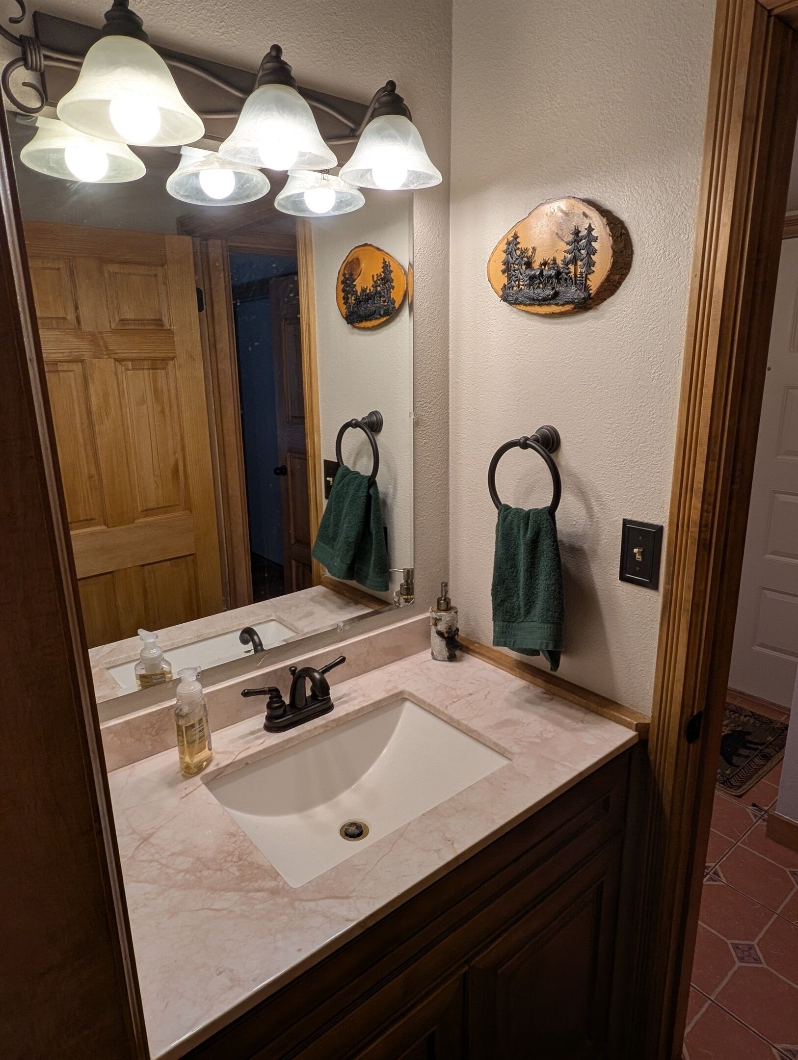 Un baño con lavamanos de mármol, un espejo y tres luces empotradas en la pared. Hay dos toallas colgadas en aros para toallas y un plato decorativo en la pared.