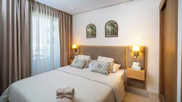 Una habitación de hotel con una cama grande, dos lámparas fijadas a la pared y un ventanal con cortinas.