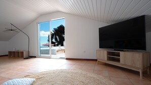 A spacious living room with a large TV, wooden cabinets, a woven rug, and a sliding glass door leading to a balcony. - Amaro Oasis by LovelyStay (Funchal)